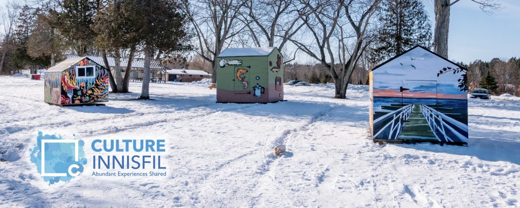 3 painted ice huts spread across a park covered in snow.