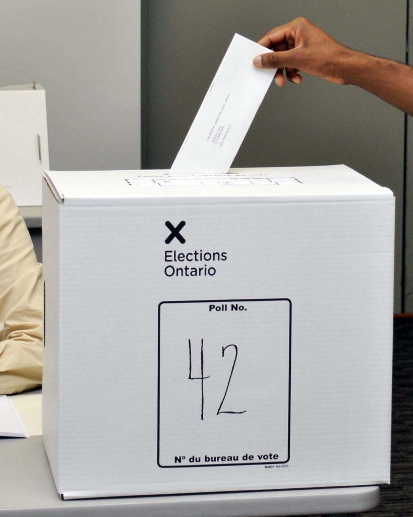 hand placing a ballot in an elections ontario ballot box