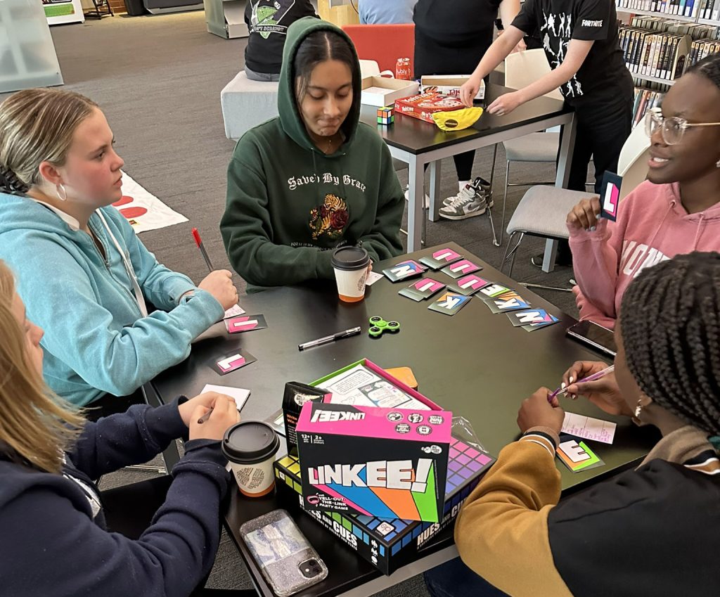 Teens gathered around a table playing a card game.