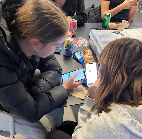 Two teens looking at their phones at a table.